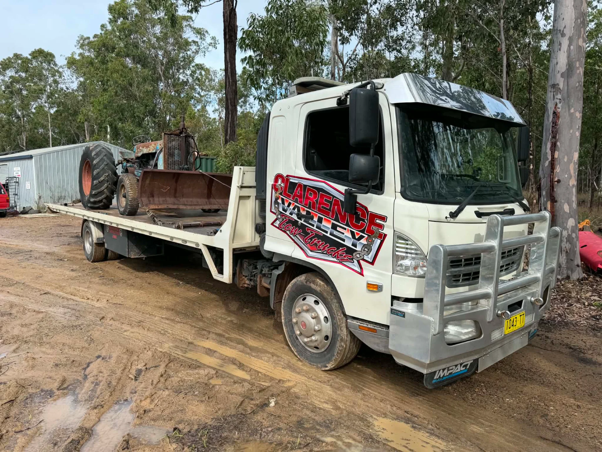 Old machinery loaded on the tilt tray on a dirt clearing