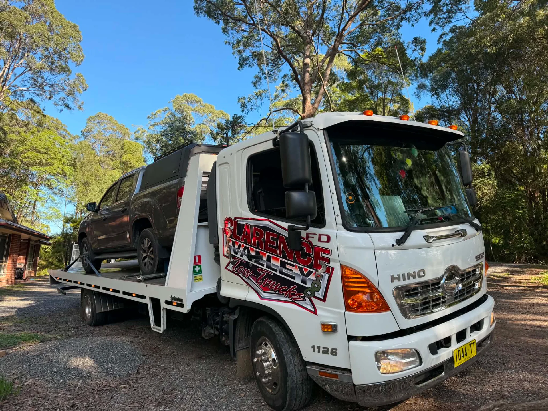 A black four-wheel drive loaded on the tilt tray under tall trees