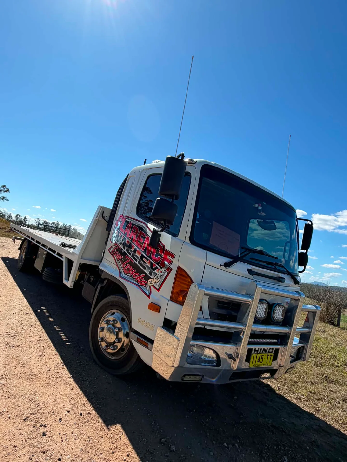 Tow truck with empty tray on red dirt under a clear sunny sky
