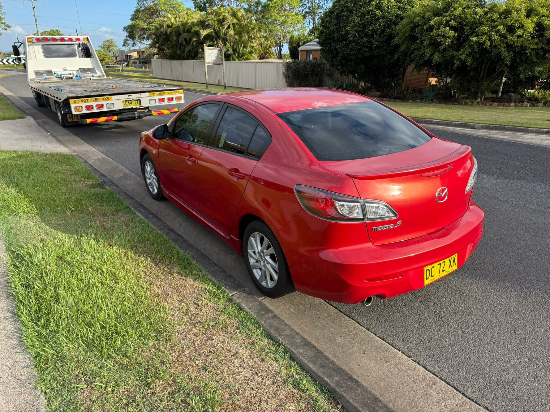 Red Mazda hatchback kerbside with a Clarence Valley Tow Trucks tilt tray attending a lockout callout