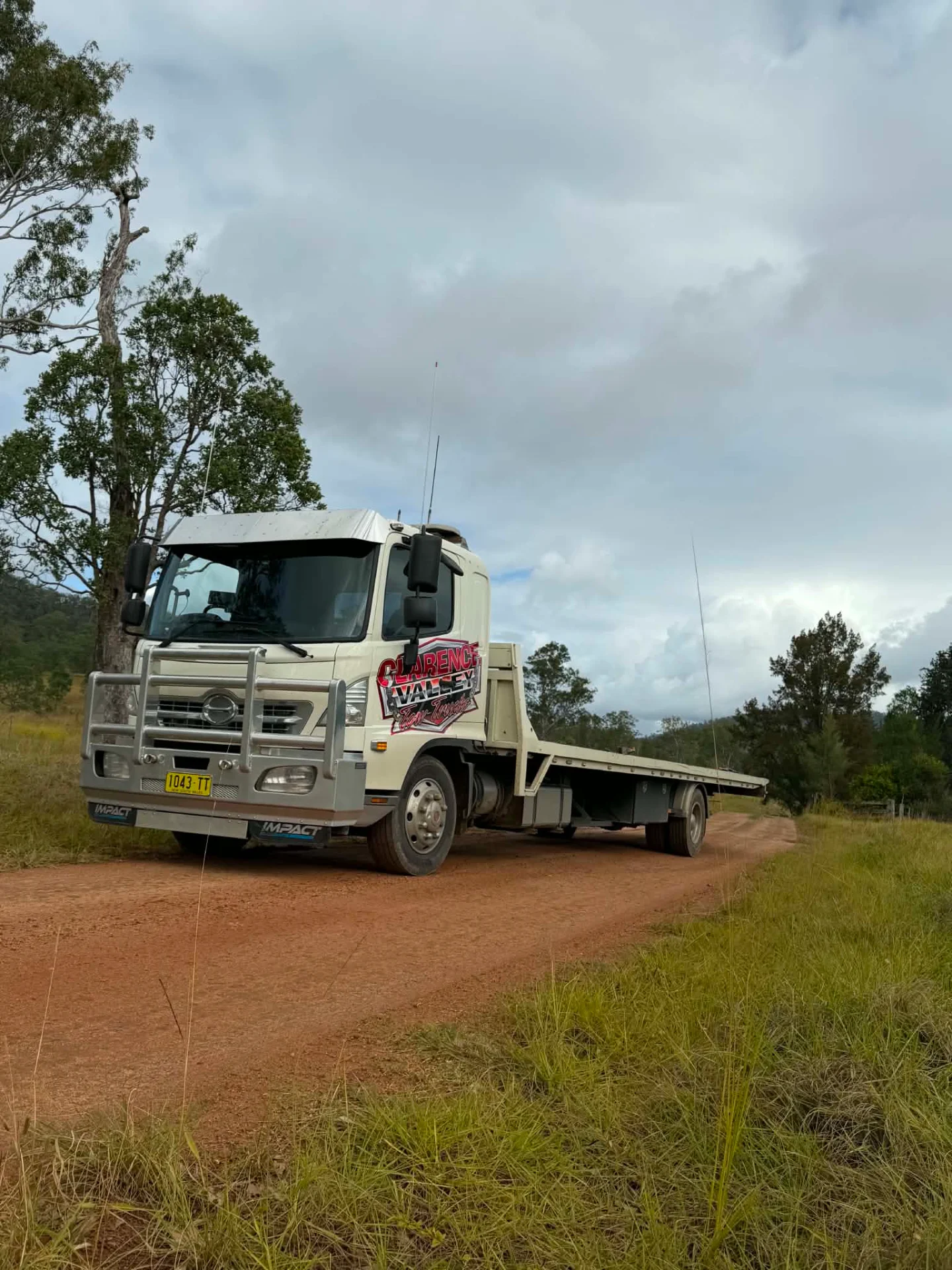 Tow truck with an empty tray on a red dirt road lined with gum trees