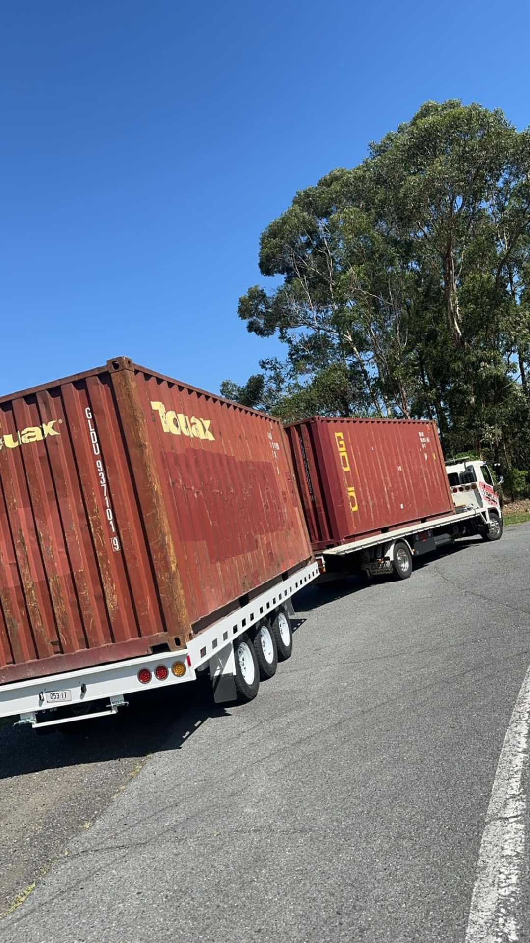 Two red shipping containers loaded on Clarence Valley Tow Trucks tilt trays parked roadside