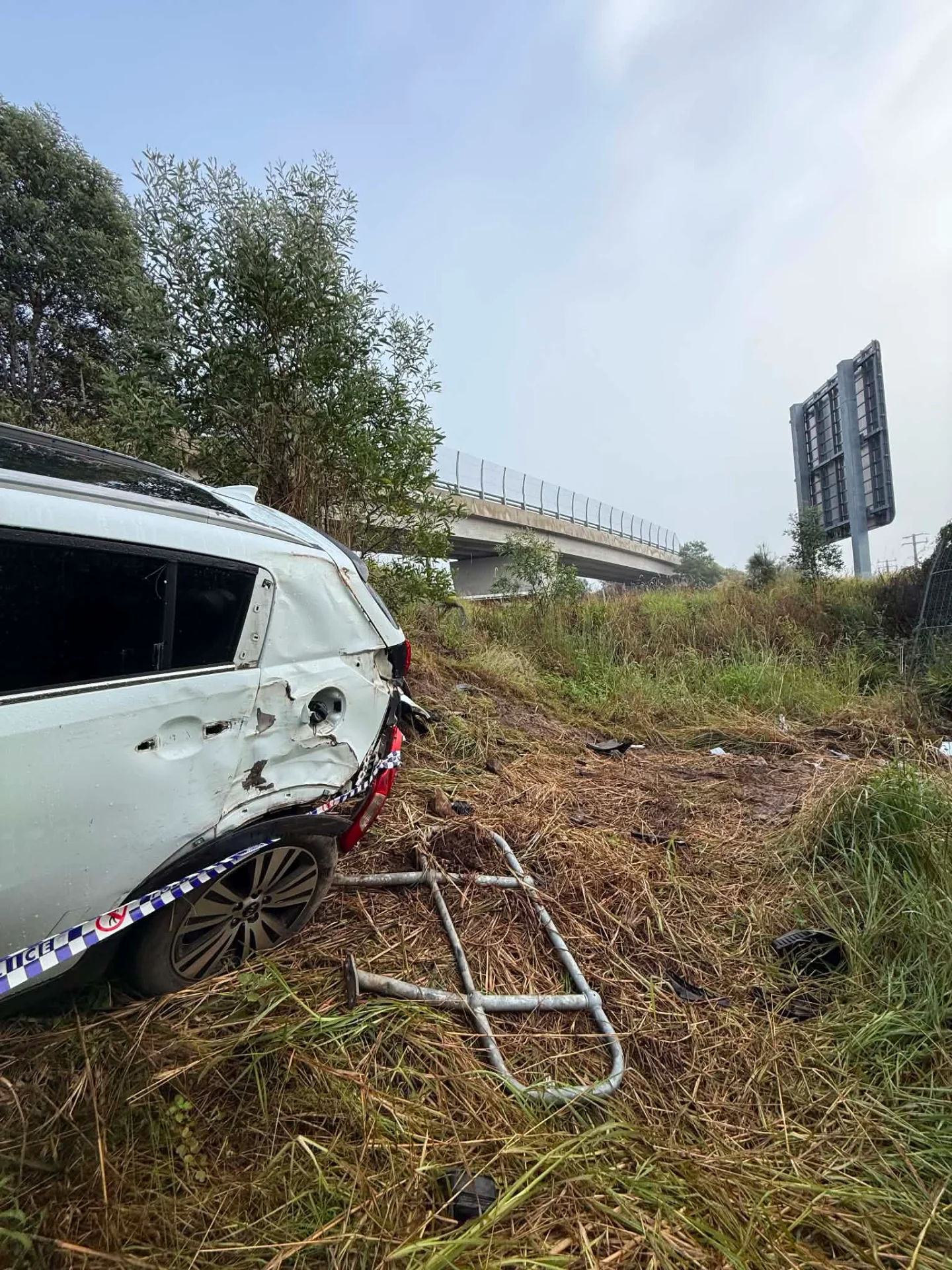 A crashed white four-wheel drive in long grass beside a highway with police tape