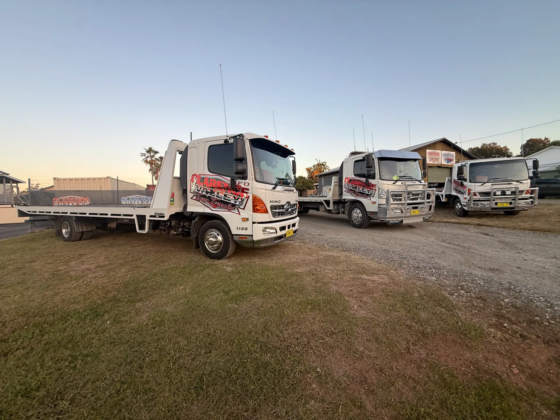 Tow trucks parked on grass beside the depot as the sun goes down