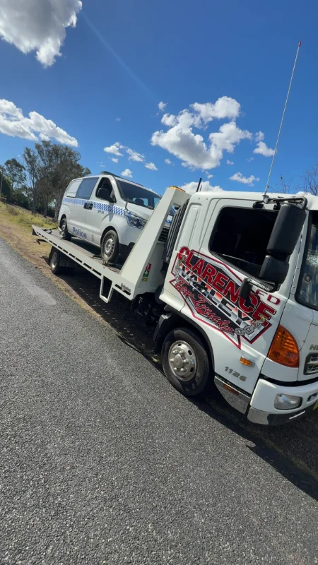 A white van winched onto the tilt tray under a bright blue sky