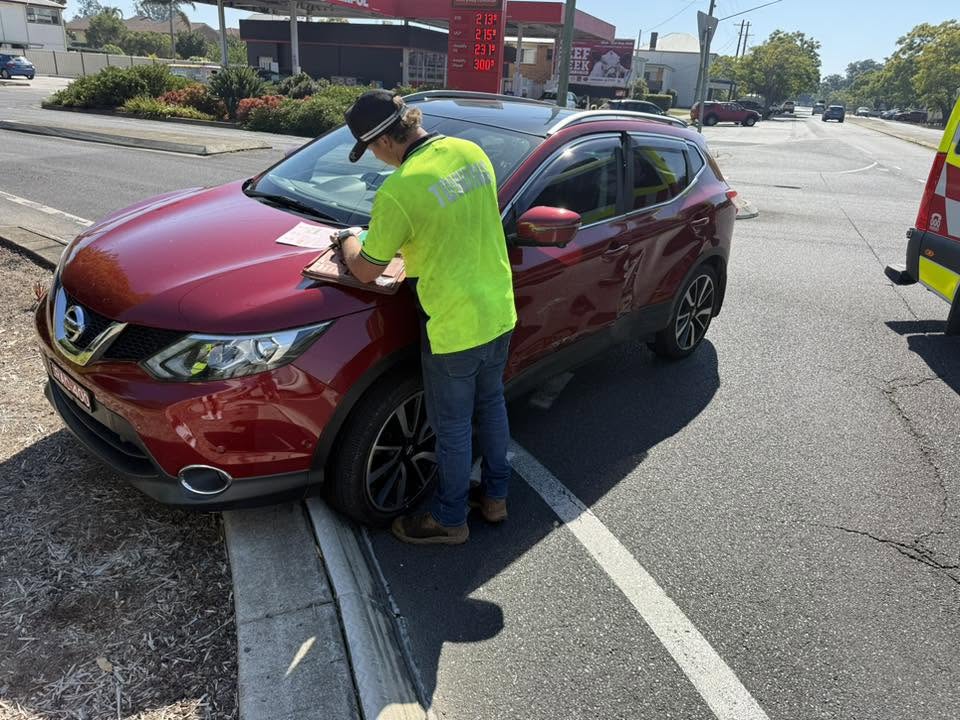 Clarence Valley Tow Trucks operator recording accident towing details beside a crash-damaged red SUV