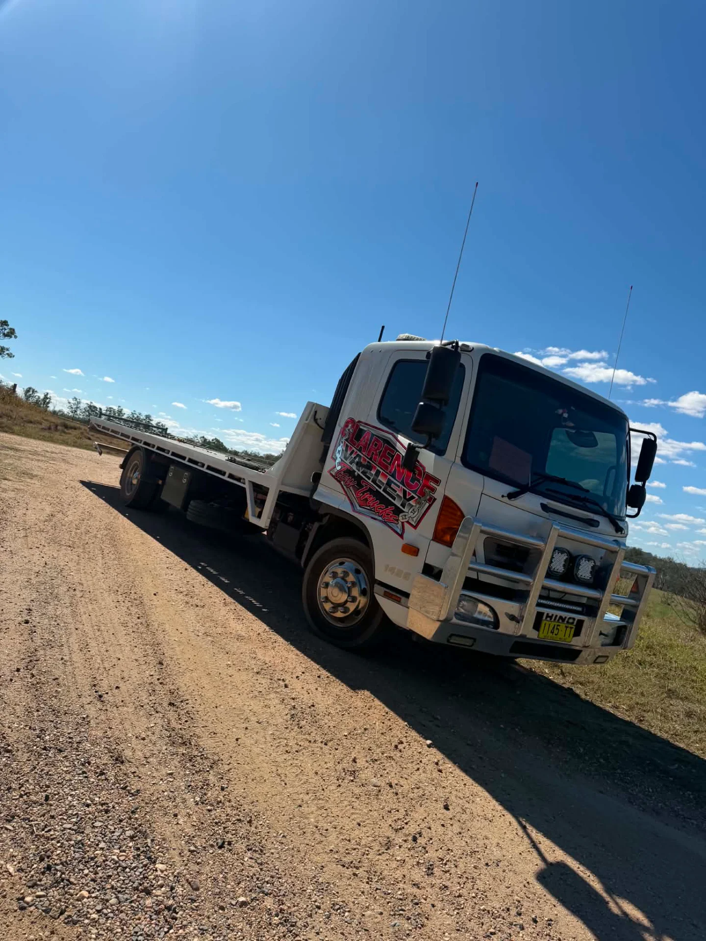 Tow truck with an empty tray on a gravel road under clear blue sky