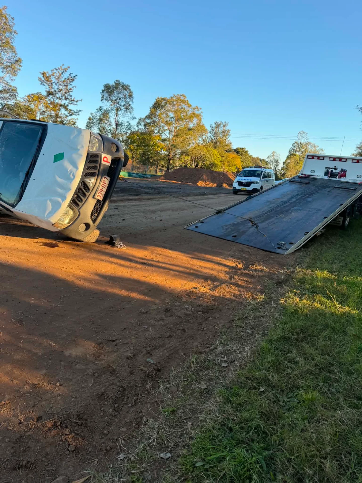 An overturned truck on a roadside verge with the tilt tray set up to recover it