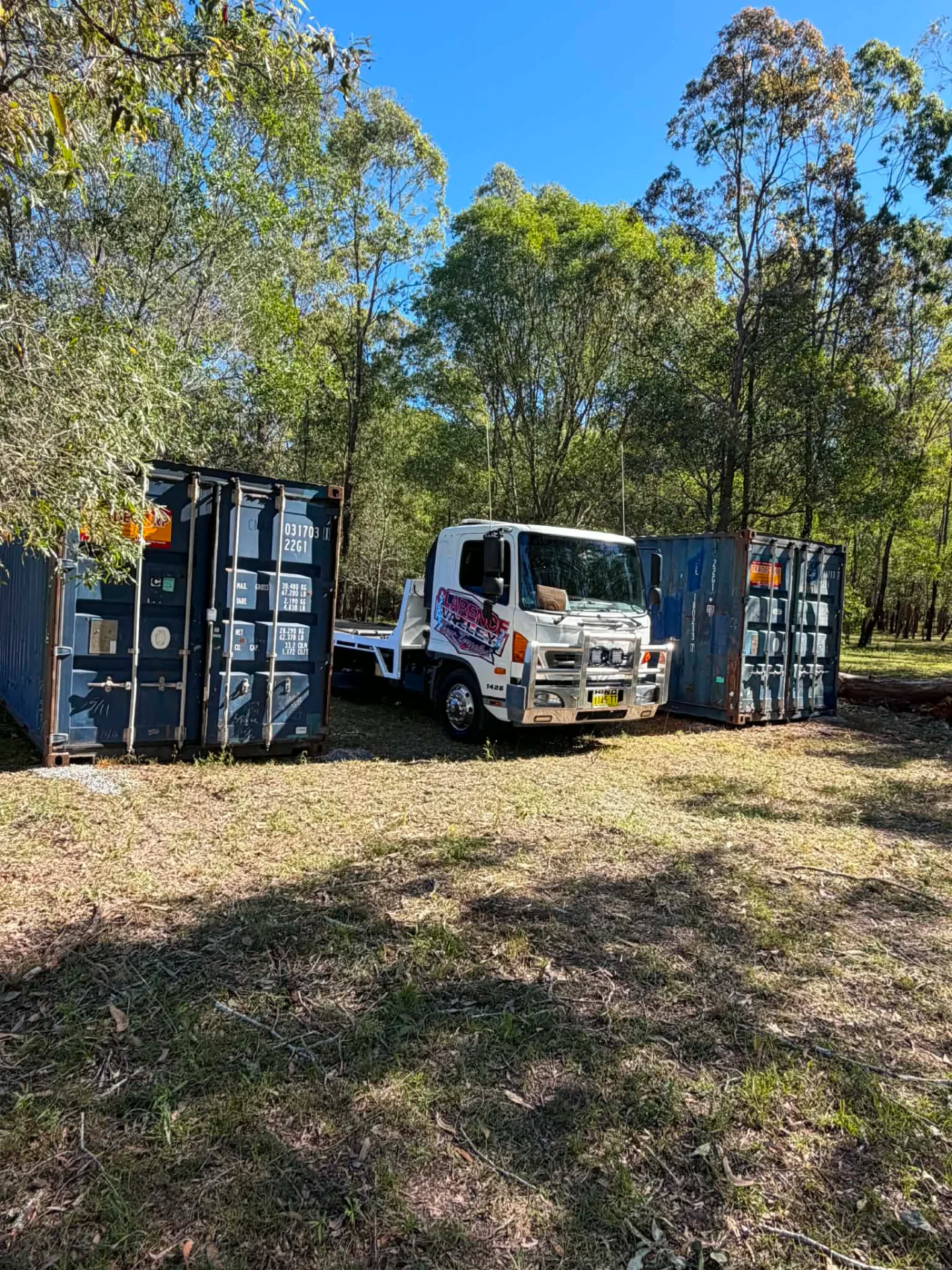 Tow truck parked between two shipping containers on a bush block