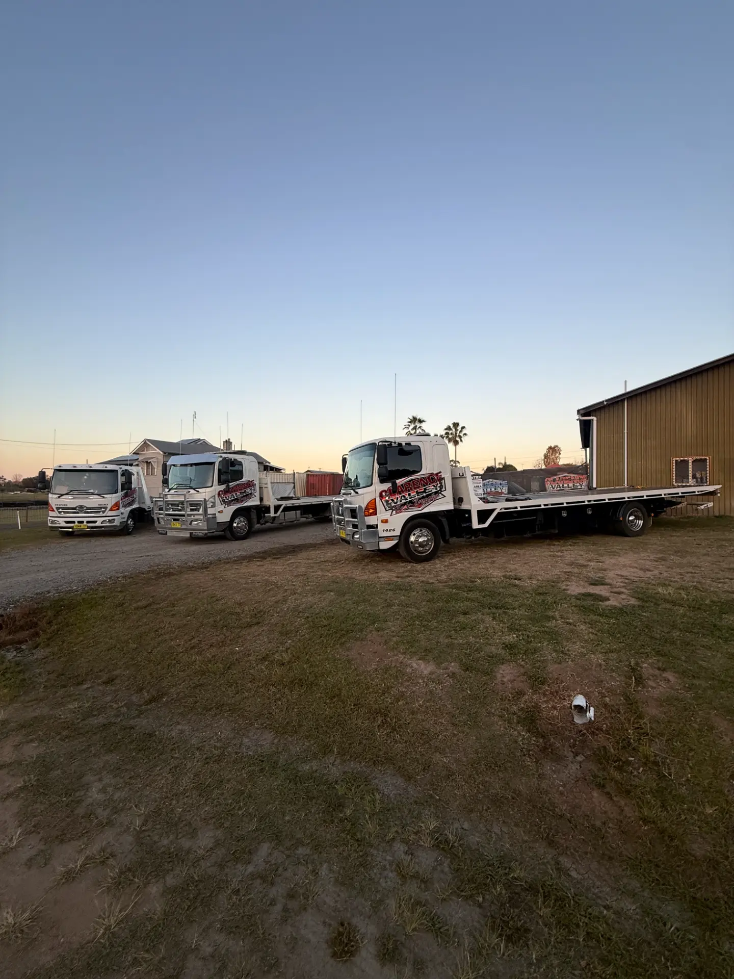 Tilt tray truck beside the depot shed with the fleet behind it at sunset
