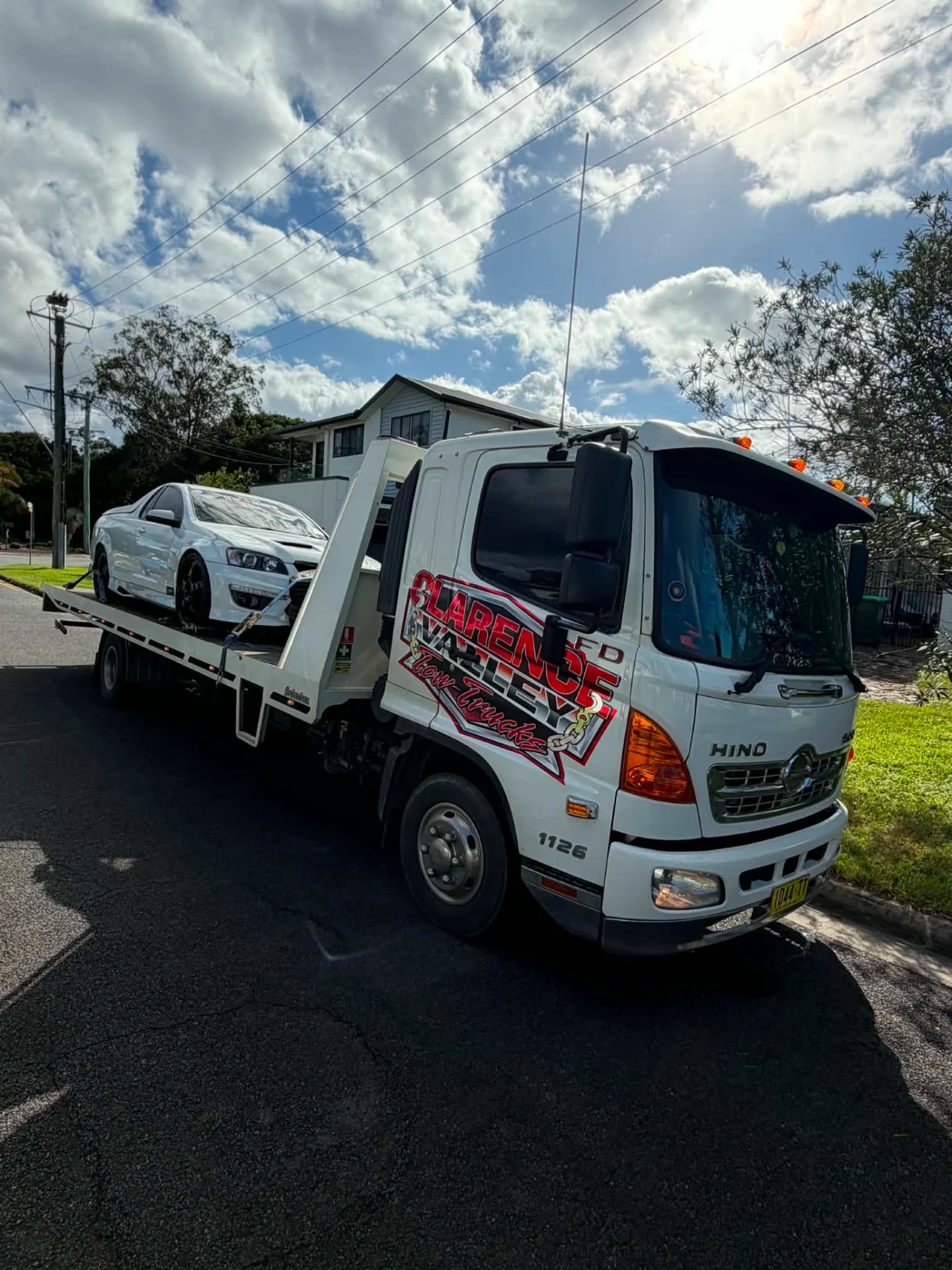 White sedan loaded on the tilt tray in a suburban street under broken cloud