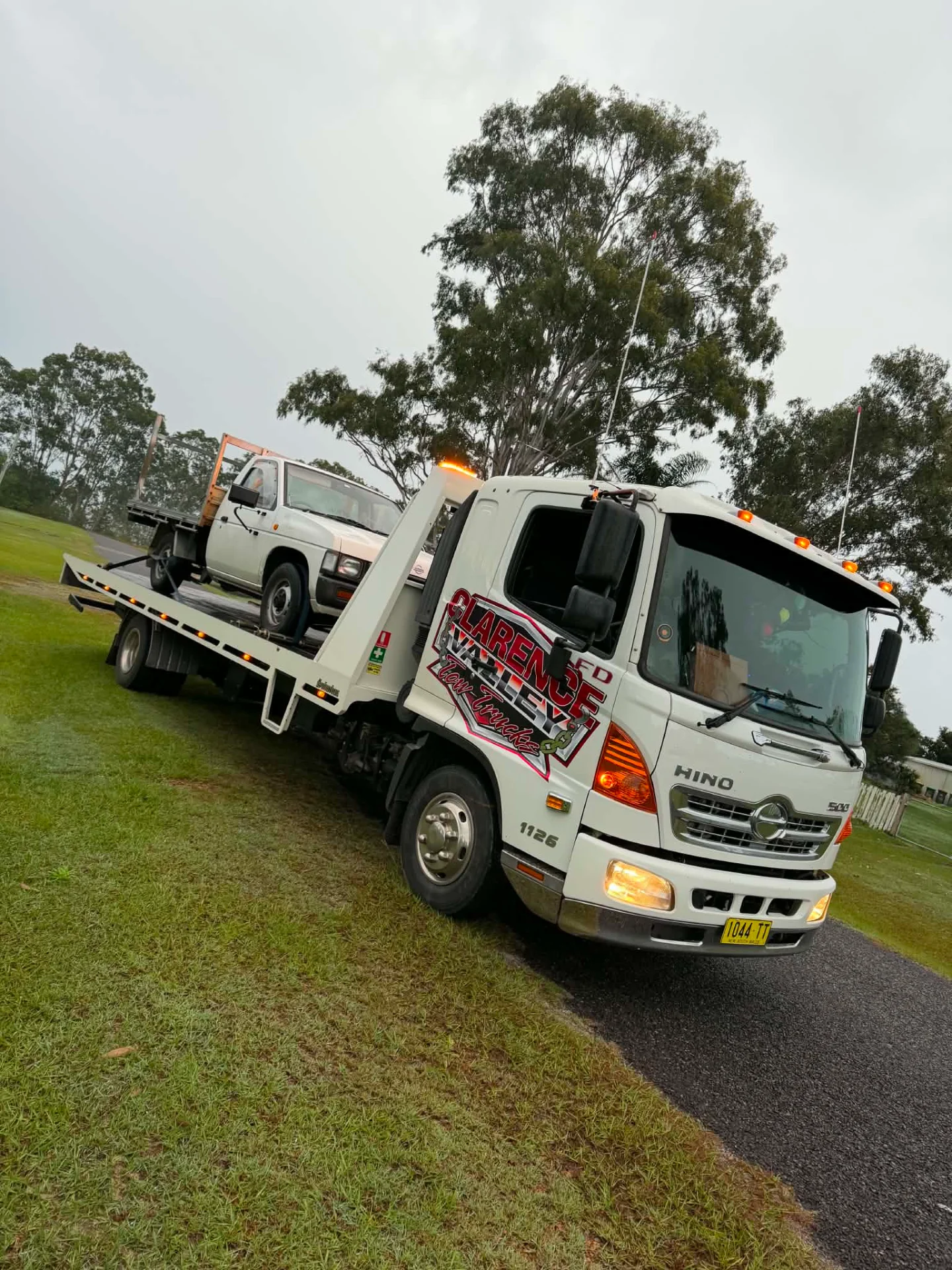 A white ute on the tilt tray parked on a grass verge
